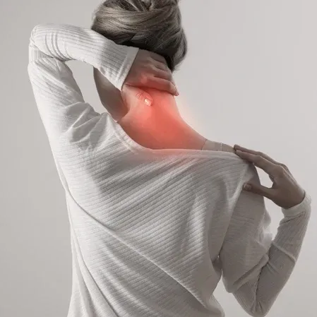 Person viewed from behind holding the neck with one hand, wearing a light sweater, with a red highlighted area on the neck.
